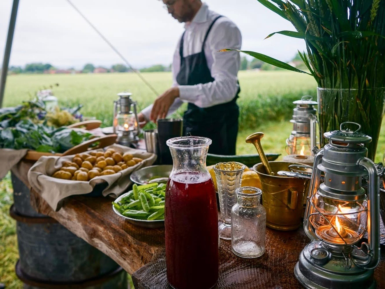 Matlagning utomhus med råvaror och grönskande äng i bakgrunden.